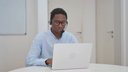 Man Wearing Headset Typing on Laptop in Office
