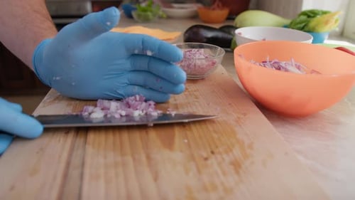Man Slicing Red Onion in Kitchen with Gloves