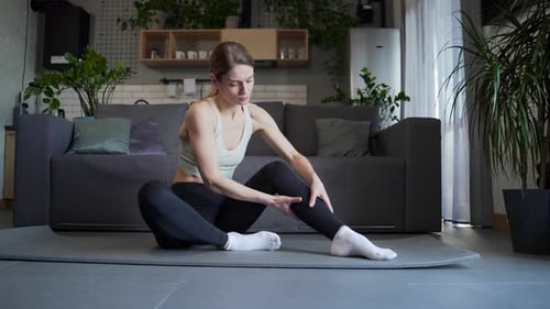 Woman Massaging Leg on Yoga Mat at Home