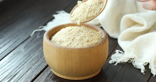 Nutritional Yeast Being Poured into Wooden Bowl