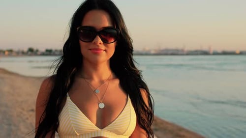 Smiling woman on beach takes off sunglasses