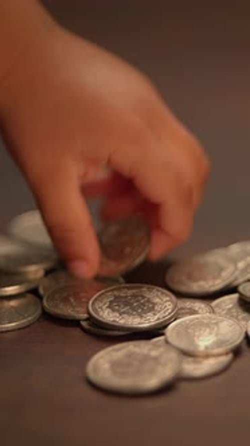 A Childs Hand Reaching Out for Coins That Are Resting on a Wooden Surface Below