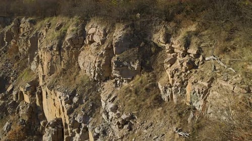 Rocky cliff with rough textures, golden sunlight, and sparse vegetation. rugged terrain highlights