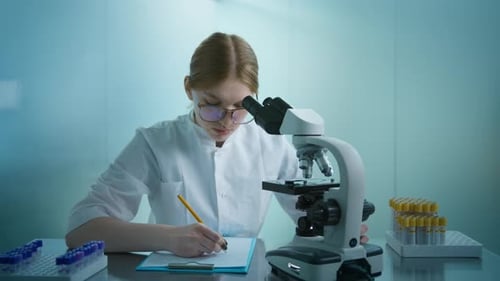 Woman Using Microscope, Recording Data in Laboratory