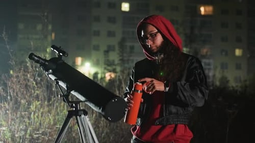 Un Stargazer à capuchon calibre son instrument au milieu d'un paysage urbain lumineux, une douce brise nocturne l'accompagne