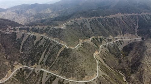 rotating aerial view: scenic road switchbacks down mountain slope