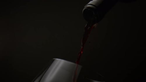 Delicious Red Wine Jet Pouring Into Crystal Wineglass From Glass Bottle On Black Background Close...