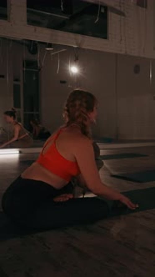Vertical screen: Women Practicing Yoga in Dimly Lit Studio