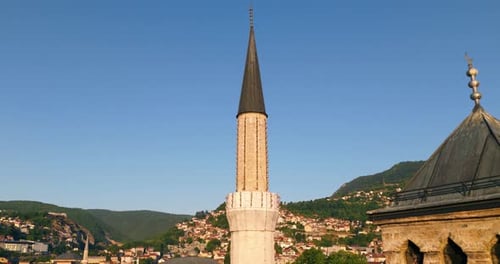 Moschee-Minarett und Glockenturm mit Bergen und Häusern am Hang in Sarajevo bei Sonnenuntergang. Pullback