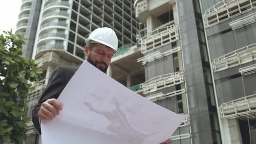 Caucasian Confident Industrial Specialist Uses Blueprint Drawings of the Plan Present in the Factory