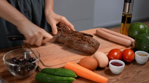 Woman cuts dark bread on wooden cutting board