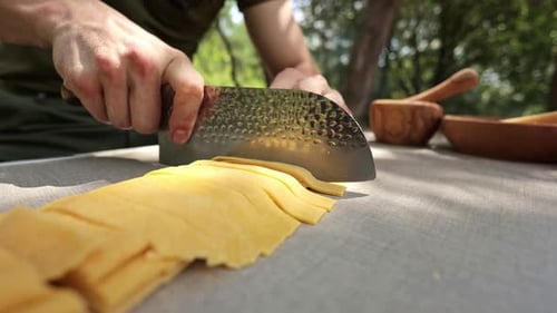 Adult Cutting Pasta with Large Knife Outdoors