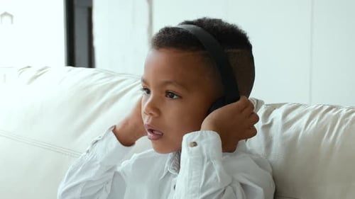 Young Boy Listening with Headphones Indoors on Sofa