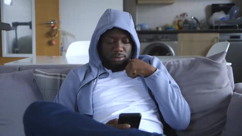 Black Male Sitting On Couch And Texting In Lounge Room