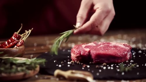 Raw Steak Being Seasoned with Rosemary Sprigs