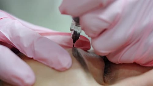 Tattoo master applies thin lines on the client’s brows. Performing beauty procedure in salon.