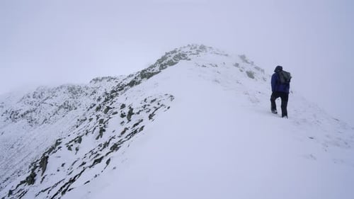 Hiker walking over mountain ridges and snow in winter time on a foggy day.