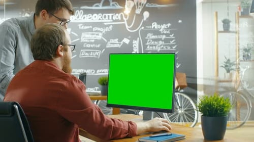 Two Male Developers Talk about Project, while Personal Computer Has Green Mock-up Screen. They Work