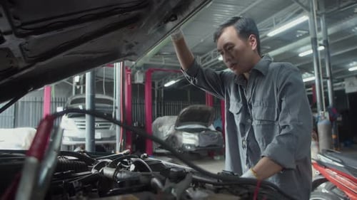 Mecánico mirando el capó abierto de un automóvil mientras trabajaba en una estación de reparación
