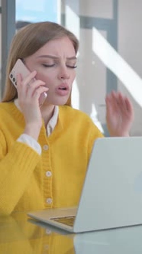 Serious Woman Talking on Phone Working on Laptop