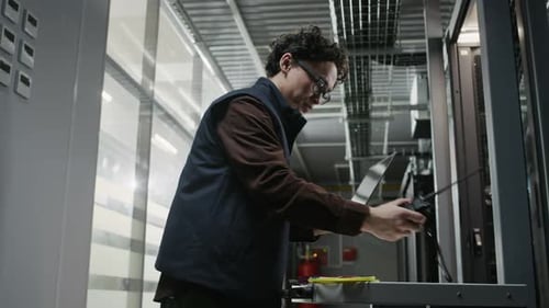 Network Engineer Communicating on Radio and Checking Laptop in Data Center