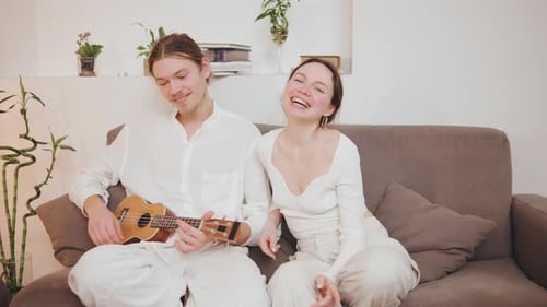 Smiling Couple Relaxing on Couch Playing Ukulele