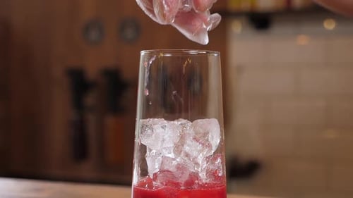 Closeup of a Bartender in Gloves Putting Ice Cubes in a Glass with Berry Juice