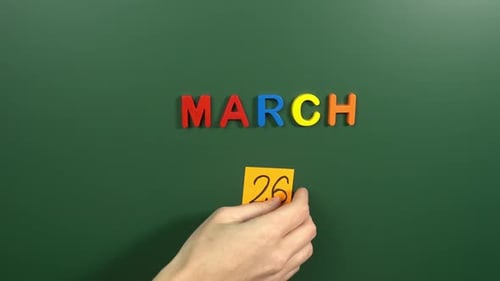 Hand sticking a sticker 26 March calendar day on school board. 26 date of March. Twenty sixth day