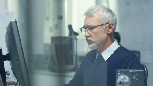 Engineering Bureau. Chief Engineer Working at His Desk, Some Technical Components Lying on His Desk