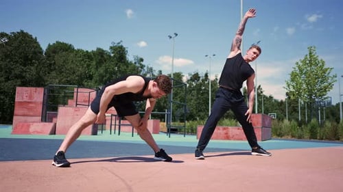 Personal fitness trainer trains athlete on sports field Two active guys train outdoors doing leg