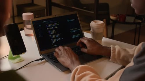 Black Man Developing Software on Laptop at White Desk in Office