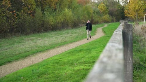 Un jeune homme en appel téléphonique marche sur un chemin de terre dans un parc en direction de la caméra