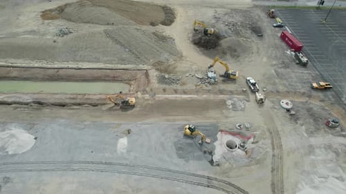 A static aerial shot of busy construction site near mall. Tractors, bulldozers and trucks are workin