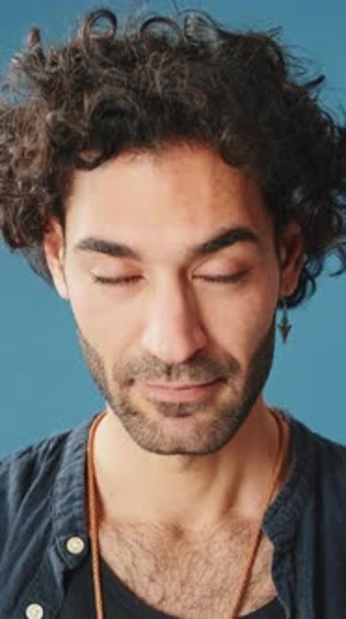 Close-up, man raises his head and looks at camera isolated on blue background in studio