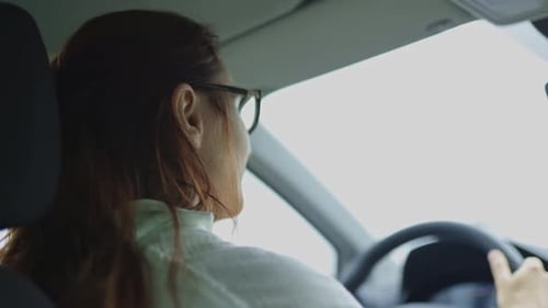 A Woman is Driving a Car and Looking at Her Reflection in the Rearview Mirror