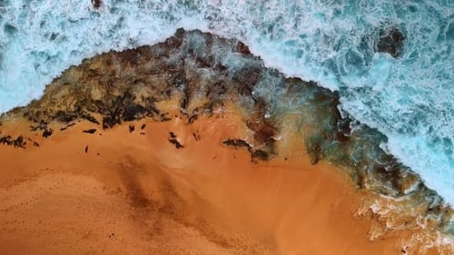White foamy waves splash on the sandy beach and rocks sticking out of shore.