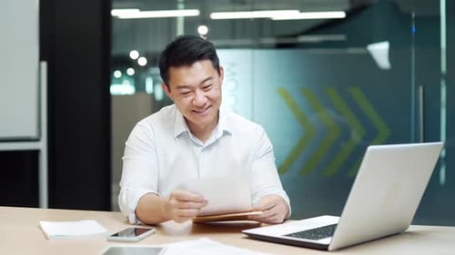 Excited satisfied asian businessman reads a document. happy glad man looking, checking at paper