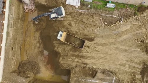 Aerial Video Aerial View of a Construction Project with an Excavator Digging and Loading Soil Into a