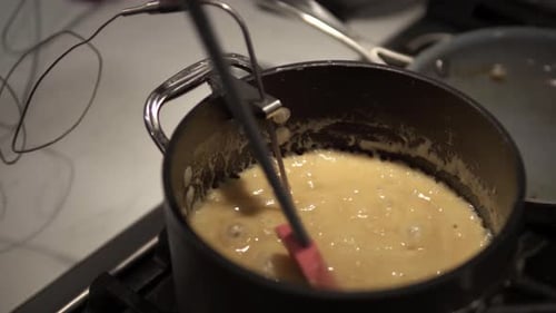 A young girl stirs a caramel mix heating up on the stove while baking millionaire shortbread cookies