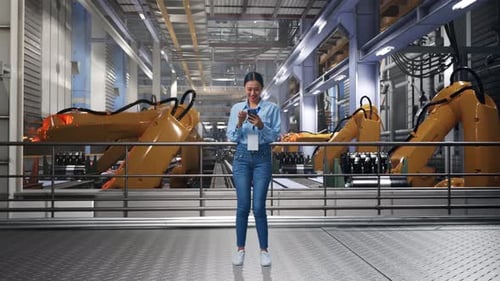 Young Woman Uses Smartphone in Robotics Factory