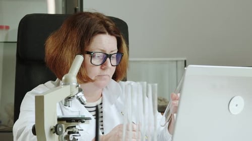 Slow Motion Woman in a White Coat Works in a Laboratory with Test Tubes and a Laptop Researcher in