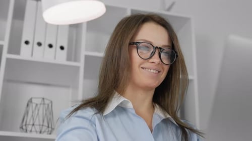 A Smiling Professional Woman Diligently Working on Her Computer Within a Modern Office Environment