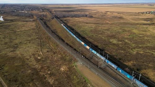 Long Freight Train is Traveling on a Railway Track Through a Vast Rural Landscape Aerial View