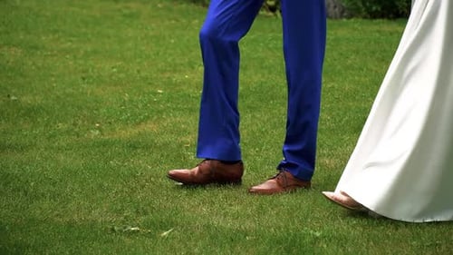 Closeup shot of the legs of bride and groom walking together on the grass in the park on the sunny w
