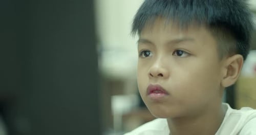 An Asian boy in elementary school is having fun using his desktop computer to play games