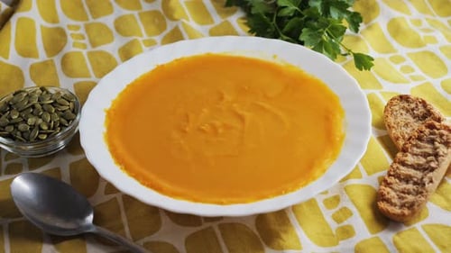 Pumpkin Cream Soup on the Table with Pumpkin Seeds Herbs and Bread