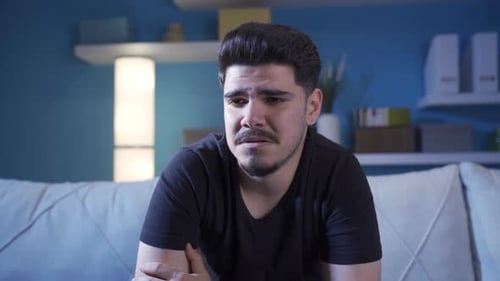 Upset Young Adult Man Sitting on Couch at Home