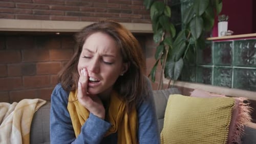 Woman Experiencing Pain and Touching Face on Sofa