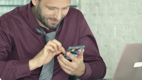 Junger Geschäftsmann schreibt SMS auf dem Smartphone und sitzt zu Hause am Tisch der 30er
