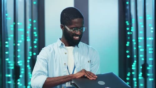 A Man Oversees Tech in a Server Room While Another Works on Data